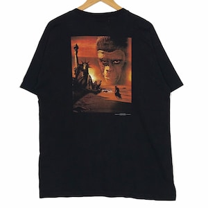 May include: Black t-shirt featuring a movie poster graphic. The graphic depicts the Statue of Liberty on a beach with a sunset backdrop and a close-up of an ape's face. The shirt is hanging on a wooden hanger.