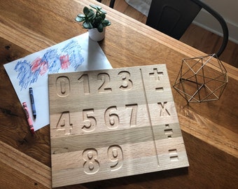 May include: Wooden learning board with the numbers 0-9 carved into the surface. The board is divided into three sections, with the numbers 0-3, 4-7, and 8-9. The board also has symbols for addition, subtraction, multiplication, and division.