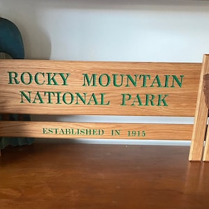 May include: A wooden sign with the text "Rocky Mountain National Park" and "Established in 1915". The sign is brown with green lettering and a brown wooden emblem.