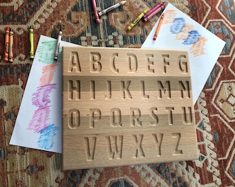 May include: Wooden alphabet board with the letters A through Z carved into the surface. The board is light brown and has a natural wood grain.