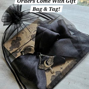 May include: A black organza gift bag tied with a satin bow. A silver charm with a crescent moon and moth design hangs from the bow. The bag contains a card with a celestial design. Text on the image reads "Orders Come With Gift Bag & Tag!"