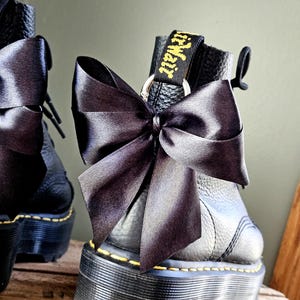 May include: Black leather platform boots with a large black satin bow. The boots feature yellow stitching and a black pull tab with the text "AirWair" in yellow.