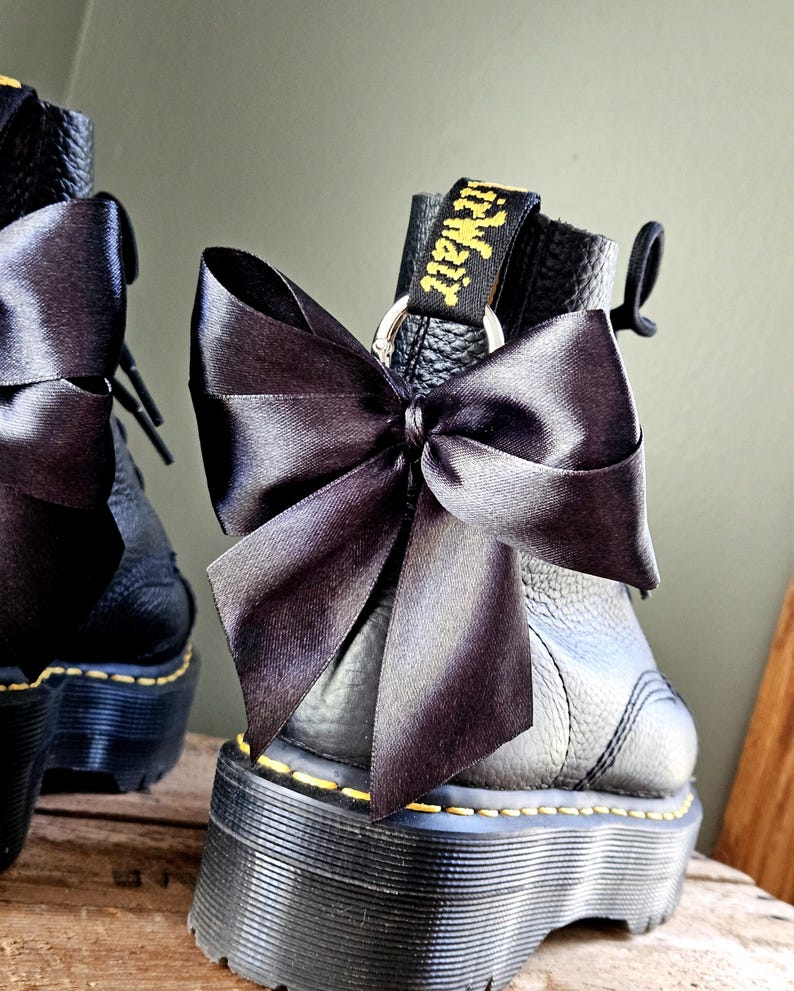 May include: Black leather platform boots with a large black satin bow. The boots feature yellow stitching and a black pull tab with the text "AirWair" in yellow.