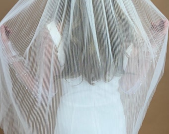 May include: A white bridal veil with a pleated design. The veil is made of a sheer fabric and has a delicate, romantic look.