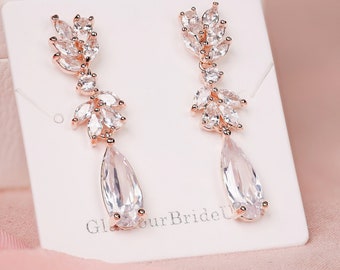 May include: Rose gold dangle earrings with clear crystal teardrop and leaf accents. The earrings are displayed on a white card with the text "Glamour Bride U".