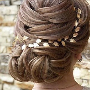 May include: A woman with a brown updo hairstyle wearing a gold leaf hair vine.
