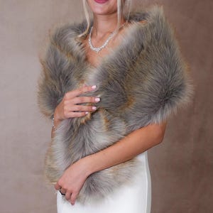 May include: A faux fur shawl in shades of gray and brown. The shawl is draped over the shoulders, creating a luxurious and elegant look. The soft, fluffy texture and neutral colors make it a versatile accessory for special occasions.
