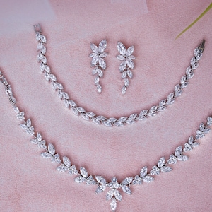 May include: A silver necklace and bracelet set with a floral design, featuring clear cubic zirconia stones. The set includes a pair of matching earrings.