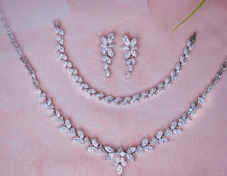 May include: A silver necklace and bracelet set with a floral design, featuring clear cubic zirconia stones. The set includes a pair of matching earrings.