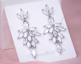 Puede incluir: Un par de pendientes colgantes de plata con piedras de cristal transparentes dispuestas en cascada en un diseño floral. Los pendientes se muestran en una tarjeta blanca con el texto "GlamourBrideSA".