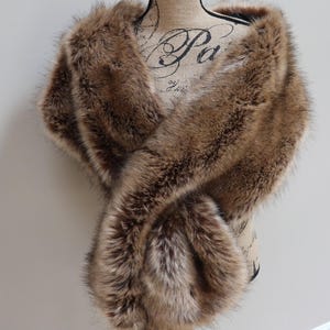 May include: A brown faux fur shawl with a long, flowing design. The shawl is draped over a mannequin and is made of soft, plush fabric.