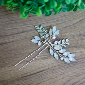 May include: Silver hair comb with blue and green leaves and white beads. The comb is on a wooden surface.