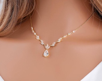 May include: A gold-tone necklace featuring a delicate chain adorned with marquise-cut clear stones arranged in a leaf-like pattern, culminating in a central teardrop-shaped pendant set with a single clear stone at the base of the design.