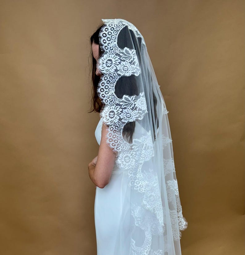 May include: A white bridal veil with a delicate lace trim featuring floral designs. The veil is made of soft tulle and has a scalloped edge.