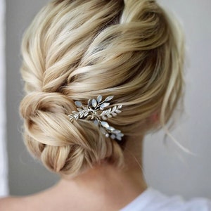 May include: A blonde woman with a low bun hairstyle adorned with a silver and crystal leaf hair comb.