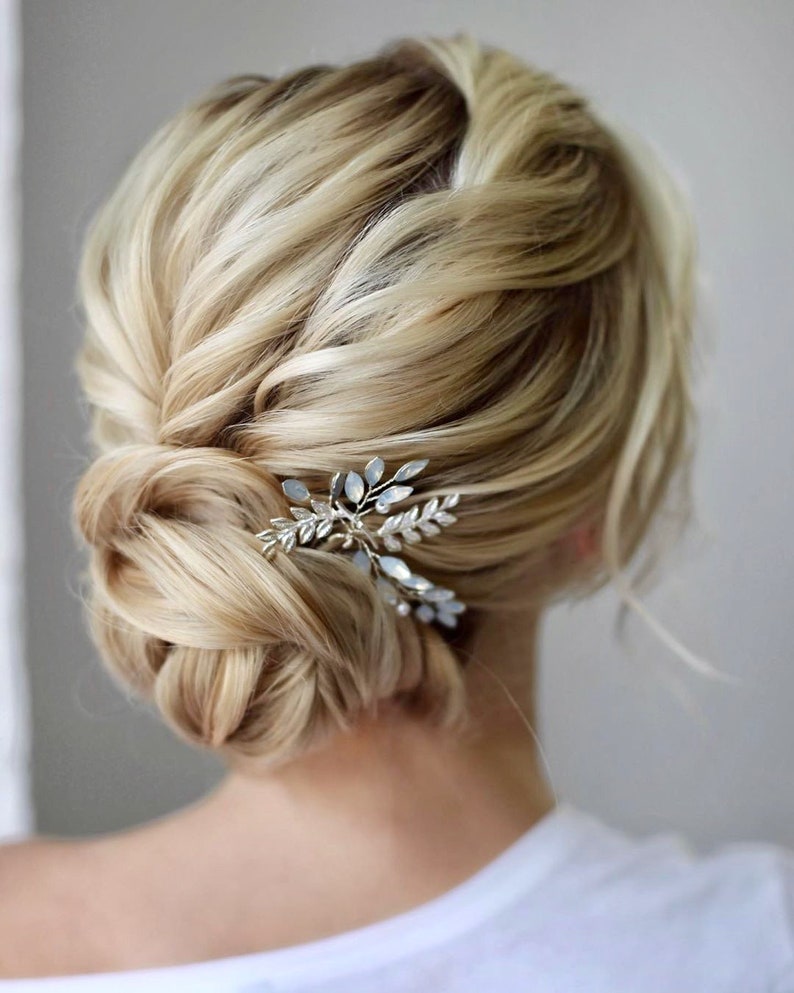 May include: A blonde woman with a low bun hairstyle adorned with a silver and crystal leaf hair comb.