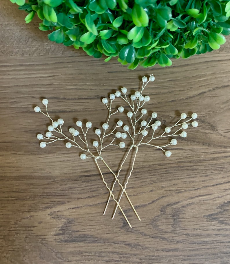 Puede incluir: Dos horquillas de pelo plateadas con detalles de perlas. Las horquillas est&aacute;n dispuestas en forma de cruz y tienen un dise&ntilde;o floral delicado.