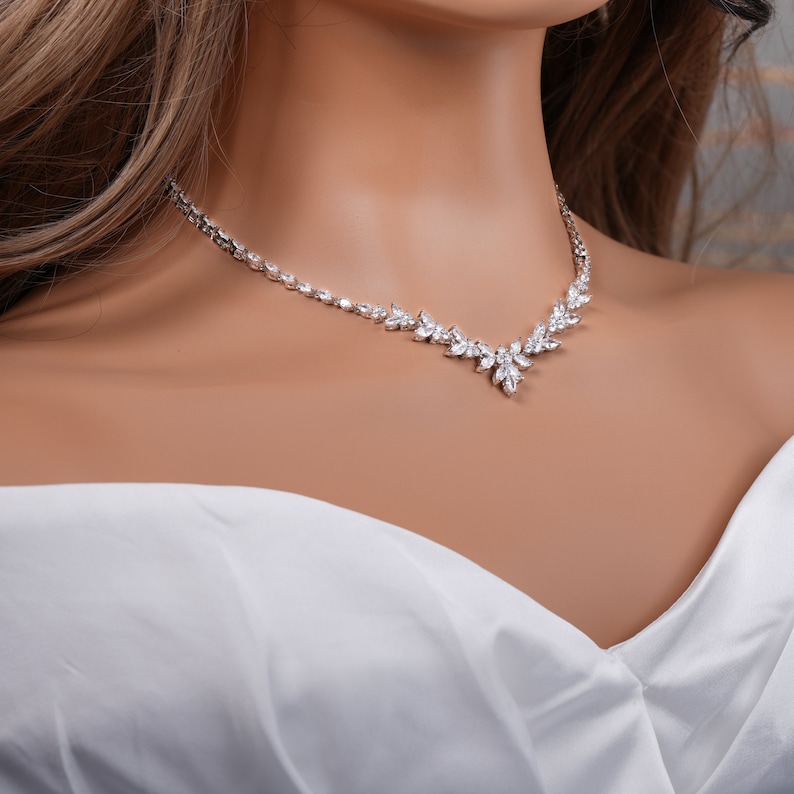 May include: A silver necklace with a delicate floral design featuring clear cubic zirconia stones.
