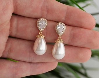 May include: Gold-coloured drop earrings with a pear-shaped, faux pearl pendant. The earrings have a teardrop-shaped, clear crystal top, surrounded by smaller crystals. The earrings are designed for pierced ears.