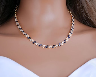 May include: A gold-toned necklace featuring a repeating leaf-like pattern composed of alternating marquise-cut deep blue and clear white stones. The chain is constructed from connected metal links that form a continuous vine-inspired design.