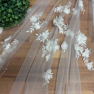 May include: White tulle fabric with white 3D floral appliques and pearl embellishments.