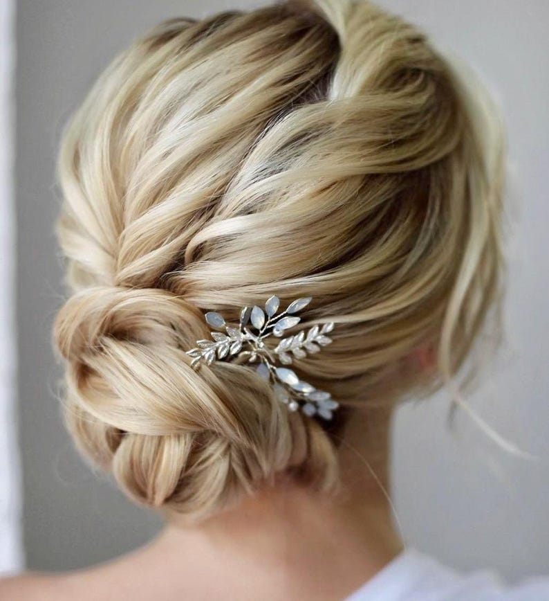 May include: A blonde woman with a low bun hairstyle adorned with a silver hair comb featuring a delicate leaf design.