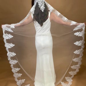 May include: A white bridal veil with a delicate lace trim. The veil is long and flowing, with a scalloped edge. The lace is intricate and detailed, with floral motifs.