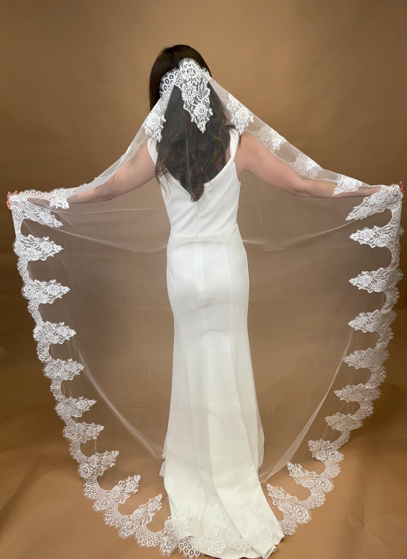 May include: A white bridal veil with a delicate lace trim. The veil is long and flowing, with a scalloped edge. The lace is intricate and detailed, with floral motifs.