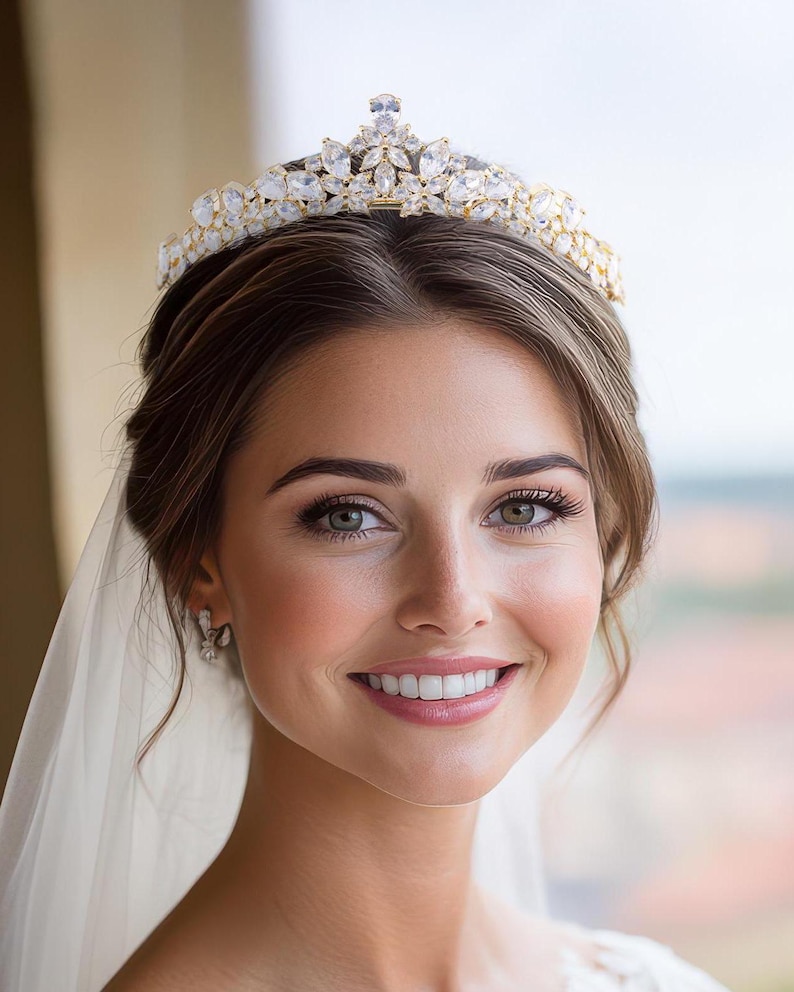 May include: A gold-toned tiara featuring a symmetrical arrangement of marquise-cut and pear-shaped clear crystals. The headpiece displays a central elevated peak with smaller flanking points, all set in a metallic frame with intricate floral-inspired metalwork.