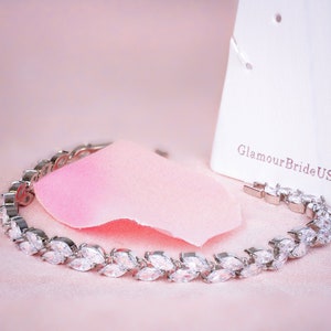May include: A silver bracelet with marquise-shaped clear stones set in a leaf design. The bracelet is on a pink background with a white tag that says "GlamourBrideUS".