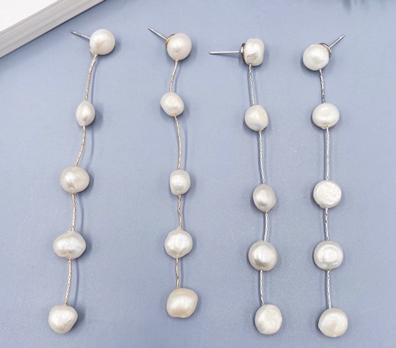 May include: Four pairs of long, silver chain earrings with white pearl beads. Each earring has a small pearl at the top and five larger pearls hanging down the chain.