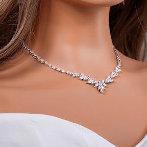 May include: A silver-toned necklace featuring a series of clear, faceted stones arranged in a V-shaped pattern. The design includes marquise-cut and round-cut stones that taper toward the center, creating a symmetrical, pointed focal point.