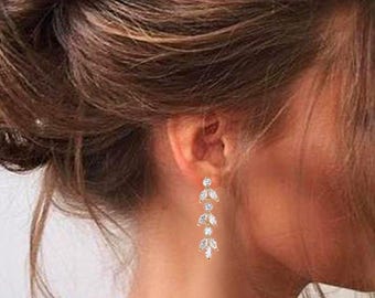May include: A gold-toned drop earring featuring a vertical arrangement of three round-cut clear stones alternating with three pairs of marquise-cut clear stones in a leaf-like pattern, suspended from a single round-cut stone stud at the top.