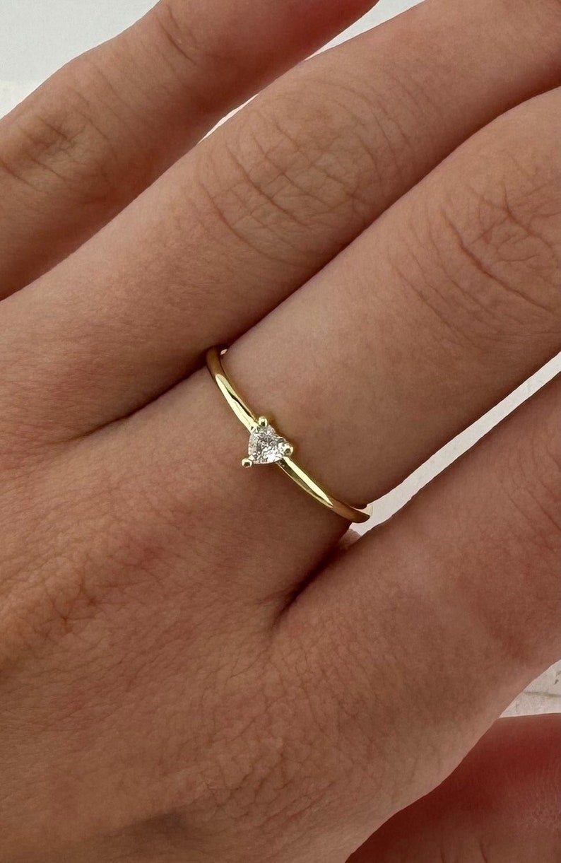 May include: A delicate gold ring with a small, clear heart-shaped stone.