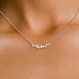 May include: A delicate silver necklace with a cluster of small, sparkling diamonds arranged in a curved line.
