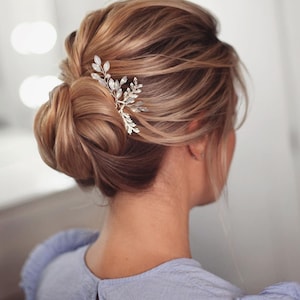 May include: A woman with light brown hair styled in a low bun with a silver and white hair comb. The comb has a leaf design with small white beads.