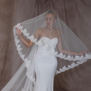 K&ouml;nnte beinhalten: Ein wei&szlig;er Brautschleier mit zarter Spitzenborte. Der transparente Schleier wird mit einem tr&auml;gerlosen wei&szlig;en Brautkleid kombiniert. Die Spitzenborte verleiht dem Brautensemble Eleganz.