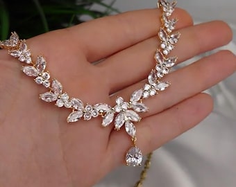 Op de afbeelding: Een gouden ketting met een delicaat, bladvormig ontwerp en een enkele, traanvormige hanger. De ketting is versierd met heldere, glinsterende stenen.