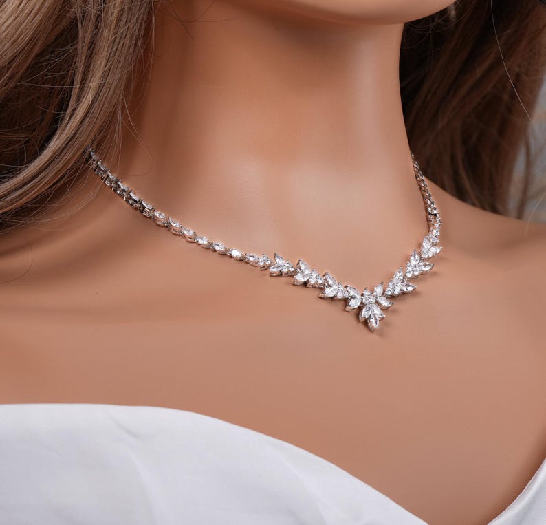 May include: A silver necklace with a delicate chain and a floral design made of clear cubic zirconia stones.