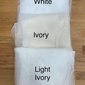 May include: Three layers of sheer tulle fabric veils arranged vertically, each featuring a delicate beaded edge. The top layer is labelled White, the middle layer is labelled Ivory, and the bottom layer is labelled Light Ivory in black text.