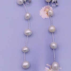 May include: A pair of long pearl earrings with clip-on closures. Each earring features a silver chain with five white pearls.