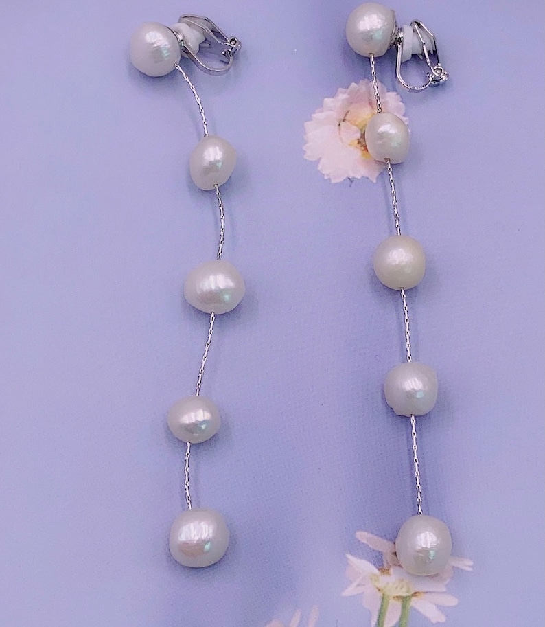 May include: A pair of long pearl earrings with clip-on closures. Each earring features a silver chain with five white pearls.