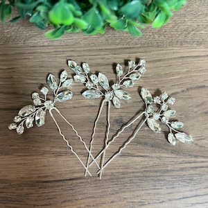 May include: Three silver-toned hair pins featuring branch-like designs adorned with clear, faceted crystals. Each pin has a two-pronged base and a decorative top section shaped like leaves and small clusters of sparkling stones arranged in a spray.