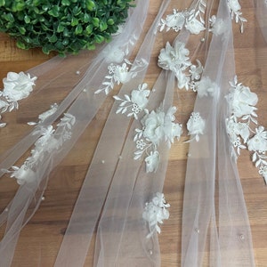 May include: White tulle fabric with 3D white floral appliques and pearl embellishments.