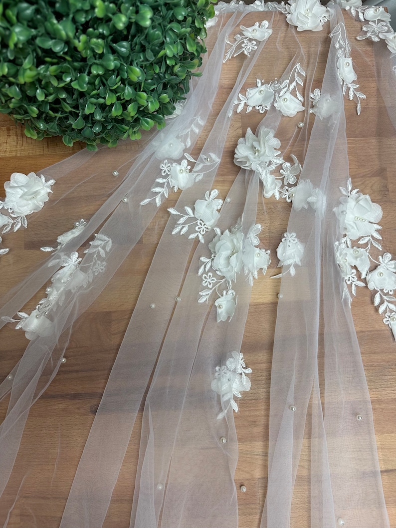 May include: White tulle fabric with 3D white floral appliques and pearl embellishments.