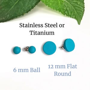 May include: Turquoise stud earrings in two styles: 6 mm ball and 12 mm flat round. The earrings are available in stainless steel or titanium. The image shows the earrings against a white background with green leaves.