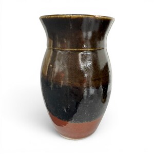 May include: A ceramic vase with a flared rim and a rounded body. The surface features a glossy glaze with a colour gradient transitioning from a dark brown at the top, through a deep black in the middle, to a warm terracotta red at the base.