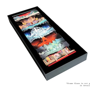 May include: A framed layered paper art piece depicting a scene with a waterfall, a mountain, a forest, and a building. The artwork is in a black frame and is displayed on a white background.
