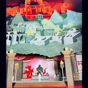 May include: A papercraft diorama depicting a fantasy city with red, green, and gray buildings. The city is surrounded by a red and green forest. Three red dragons are in the foreground, with one dragon wearing a crown.