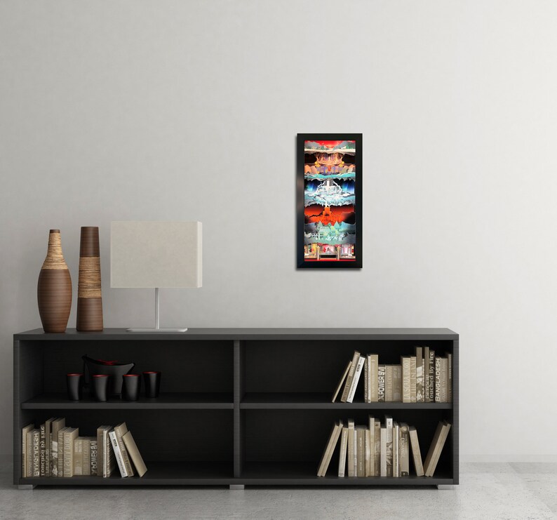 May include: A framed print of a colorful, layered illustration of a city skyline. The print is in a black frame and is hanging on a white wall above a black bookshelf.